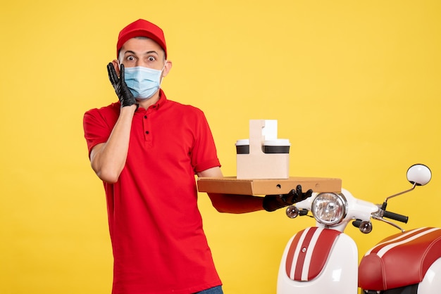 Курьер-мужчина, вид спереди в маске с доставкой кофе и коробкой на желтой службе covid - равномерная цветная вирусная работа