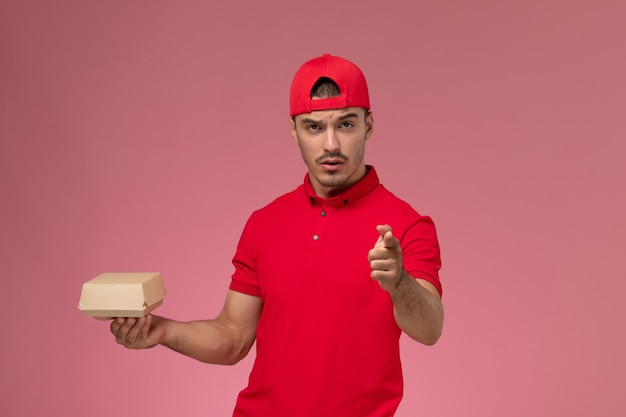 Front view of male courier in red uniform and cap holding little delivery package