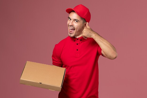 빨간색 유니폼과 케이프 핑크 벽에 포즈 음식 배달 상자를 들고 전면보기 남성 택배