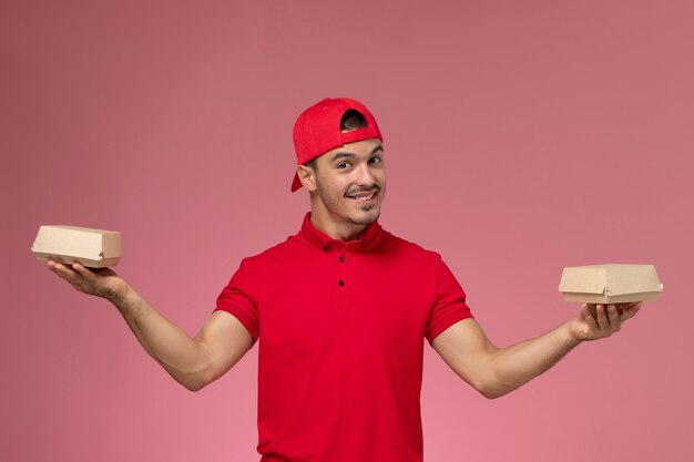 빨간색 유니폼과 케이프 분홍색 배경에 작은 배달 패키지를 들고 전면보기 남성 택배.
