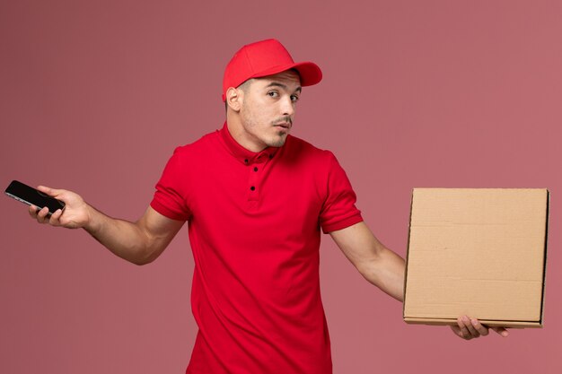 빨간색 유니폼과 케이프 핑크 벽 서비스 작업 남성 배달 유니폼에 전화 및 음식 상자를 들고 전면보기 남성 택배