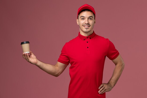 분홍색 벽 작업에 배달 커피 컵을 들고 빨간색 제복을 입은 전면보기 남성 택배