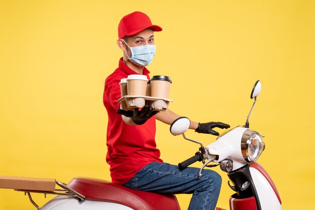 Front view male courier in red uniform and mask with coffee on the yellow color job pandemic covid- work food service virus