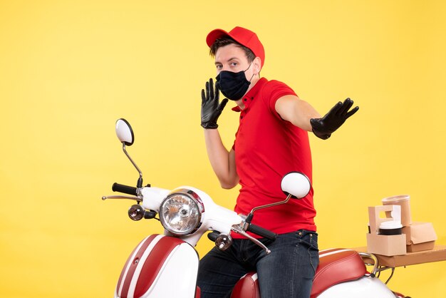 Front view male courier in red uniform and mask on a yellow 