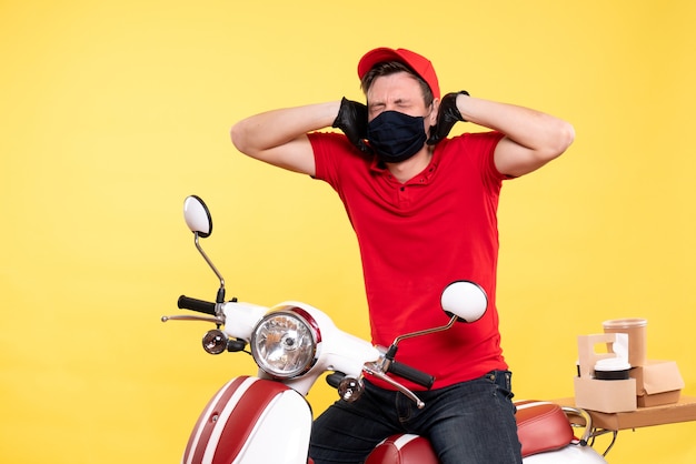 Front view male courier in red uniform and mask on yellow 