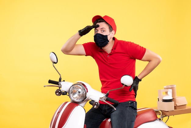 Front view male courier in red uniform and mask on yellow 