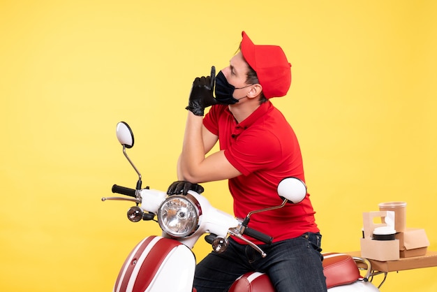 Front view male courier in red uniform and mask on yellow 