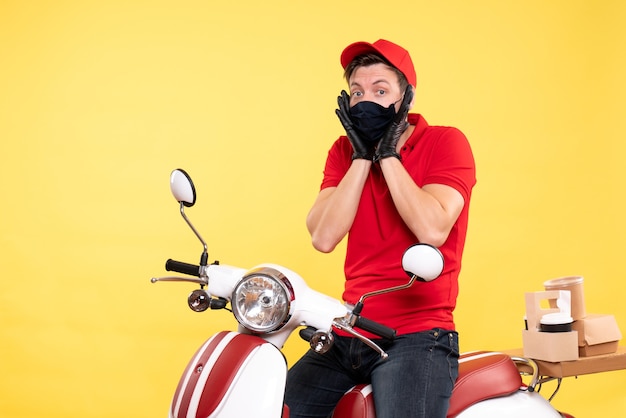 Front view male courier in red uniform and mask on yellow 