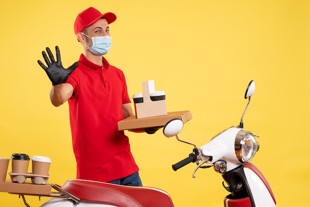 Front view male courier in red uniform with food box and coffee on yellow color covid- uniform virus work service job