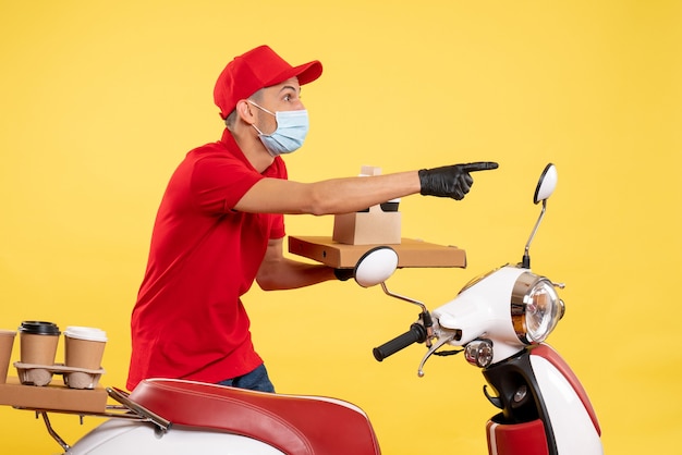 Front view male courier in red uniform with food box and coffee on yellow job service pandemic covid- uniform virus color