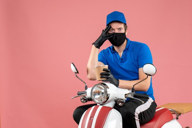 Front view male courier sitting on bike and holding big coffee cup on pink 