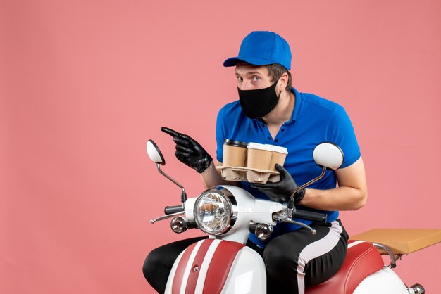 Front view male courier sitting on bike and holding coffee cups on pink 