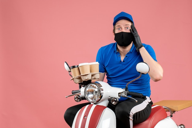 Front view male courier sitting on bike and holding coffee cups on pink 