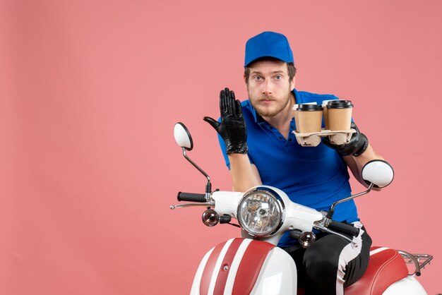 Front view male courier sitting on bike and holding coffee cups on pink 