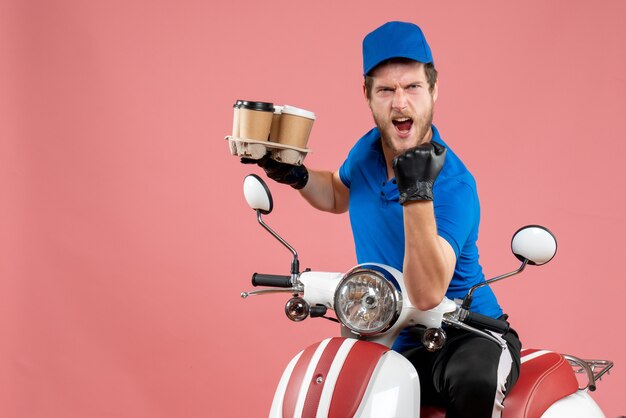 Front view male courier sitting on bike and holding coffee cups on pink 