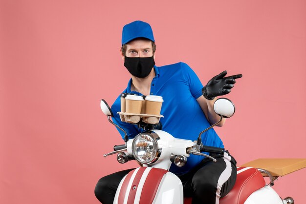 Front view male courier sitting on bike and holding coffee cups on the pink 