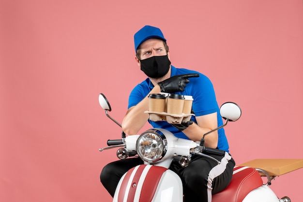 Front view male courier sitting on bike and holding coffee cups on the pink 