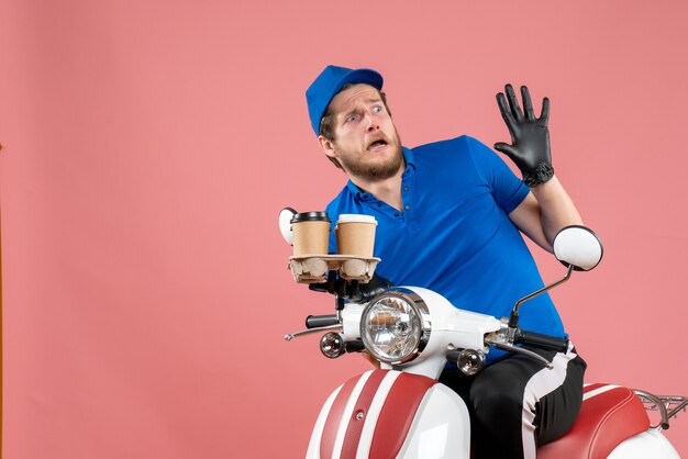 Front view male courier sitting on bike and holding coffee cups on the pink 