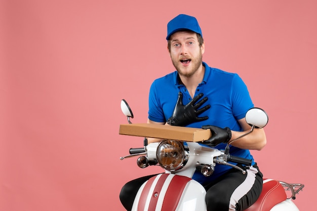 Front view male courier sitting on bike and holding pizza box on a pink 