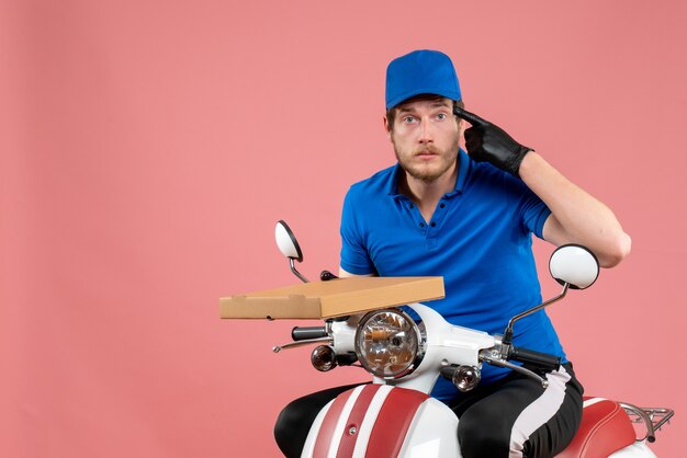 Front view male courier sitting on bike and holding pizza box on pink 