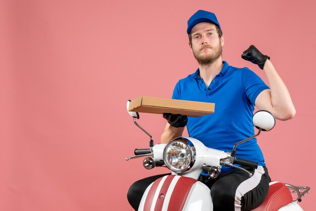 Front view male courier sitting on bike and holding pizza box on pink 