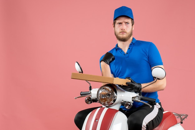 Front view male courier sitting on bike and holding pizza box on pink 