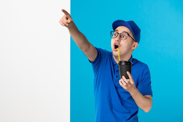 Front view male courier in uniform drinking coffee on blue 