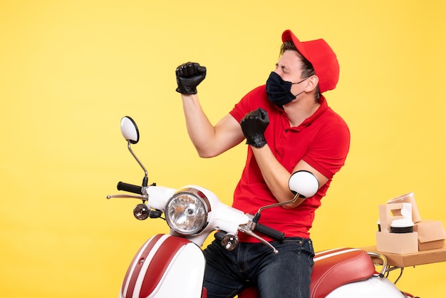 Front view male courier in uniform gloves and mask rejoicing on yellow 