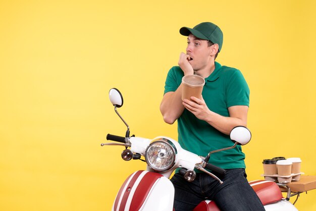 Free photo front view male courier in uniform holding coffee cup on a yellow