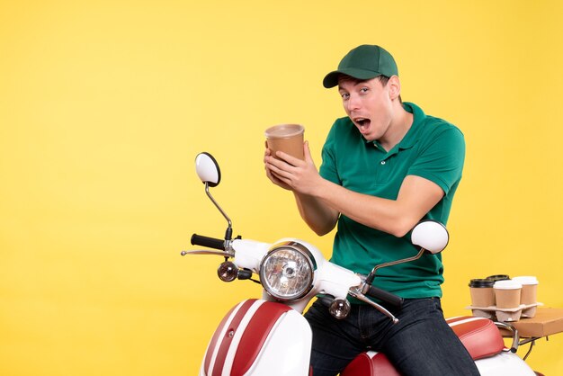 Front view male courier in uniform holding coffee cup on yellow 