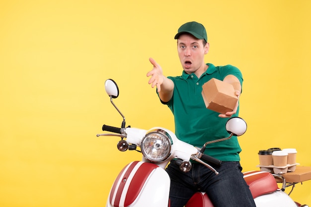 Front view male courier in uniform holding little food package on a yellow 