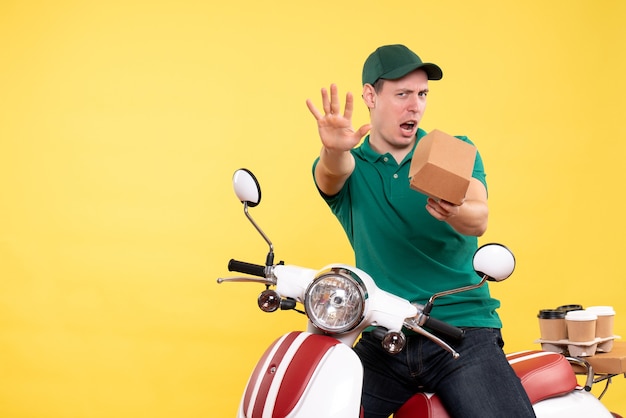 Front view male courier in uniform holding little food package on the yellow 