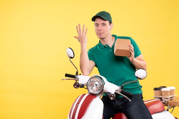 Front view male courier in uniform holding little food package on yellow 