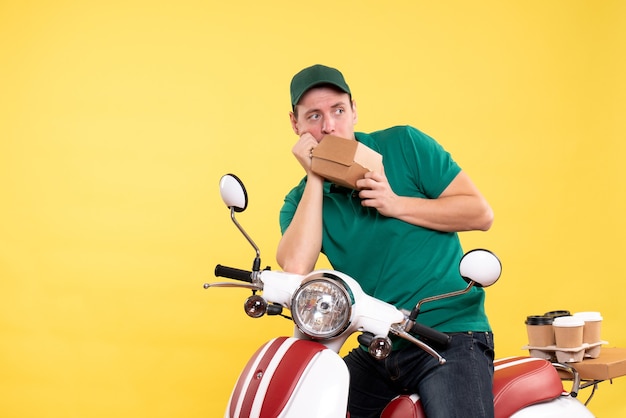 Front view male courier in uniform holding little food package on yellow 