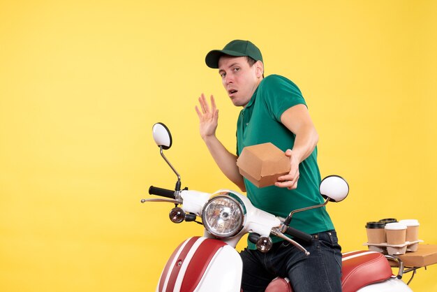 Front view male courier in uniform holding little food package on yellow 