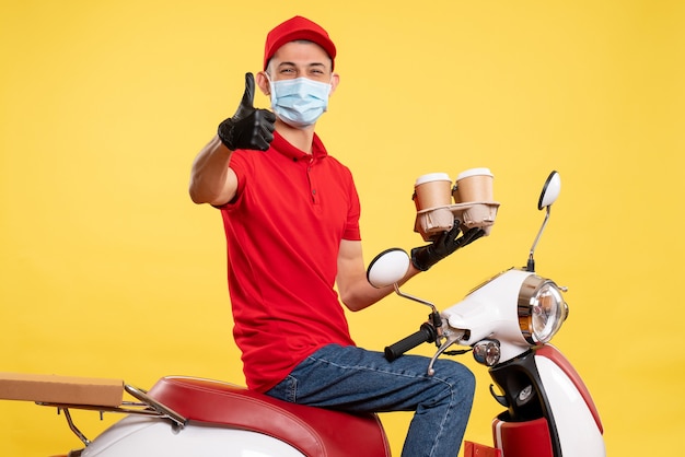 Front view male courier in uniform and mask with coffee on yellow color job pandemic covid- work service virus