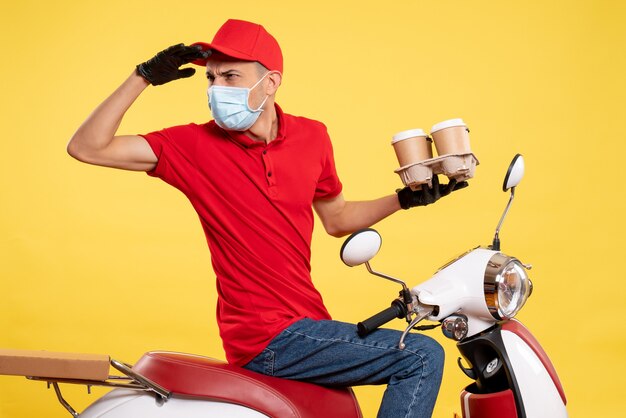 Front view male courier in uniform and mask with coffee on yellow colors job pandemic covid- work food service virus