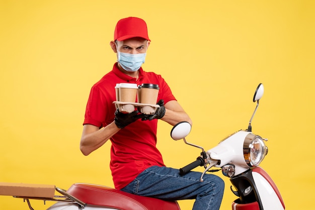 Front view male courier in uniform and mask with coffee on yellow food service job covid- virus color pandemic