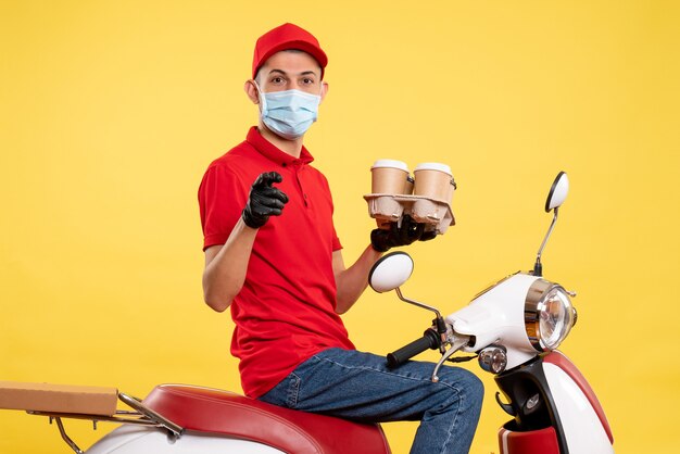 Курьер-мужчина в униформе и маске с кофе на желтом цвете, вид спереди, пандемия коронавируса, работа