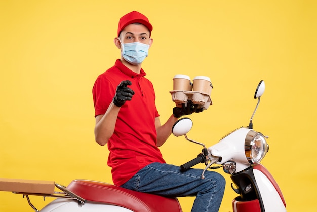 Front view male courier in uniform and mask with coffee on yellow service color job pandemic covid- virus work