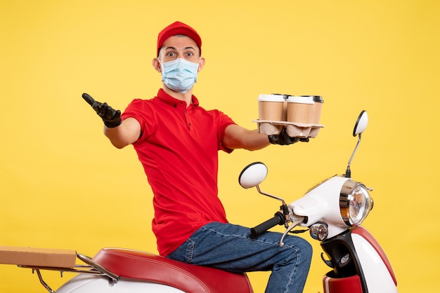 Вид спереди мужчина-курьер в униформе и маске с кофе на желтом рабочем месте службы пандемии коронавируса - пищевой вирус рабочий цвет