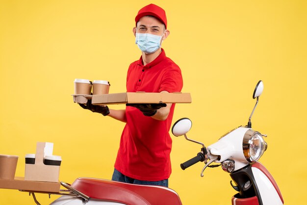 Front view male courier in uniform with coffee and food box on a yellow pandemic service work covid virus uniform color job