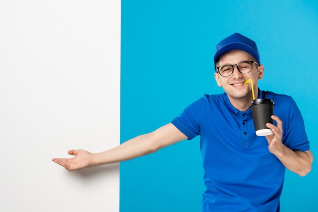 Front view of male courier in uniform with delivery coffee drinking on blue 