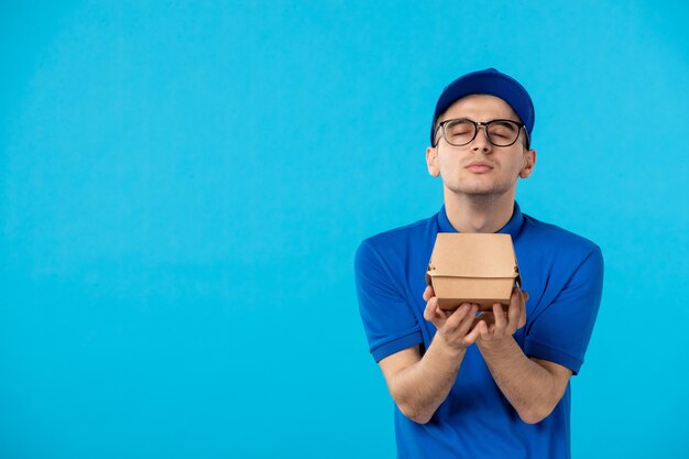 Front view male courier in uniform with food delivery package on blue 