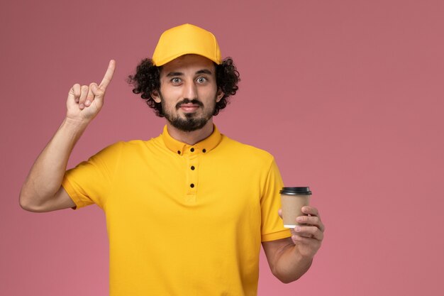 黄色の制服と淡いピンクの壁に配達コーヒーカップを保持している岬の正面図男性宅配便