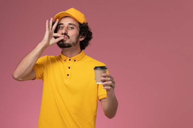 노란색 유니폼과 케이프 핑크 벽에 배달 커피 컵을 들고 전면보기 남성 택배