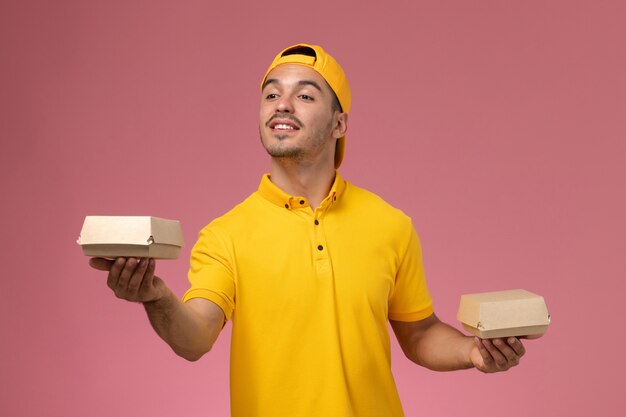 노란색 유니폼과 케이프 분홍색 배경에 작은 배달 음식 패키지를 들고 전면보기 남성 택배.
