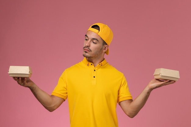 ピンクの背景に小さな配達食品パッケージを保持している黄色の制服と岬の正面図男性宅配便。