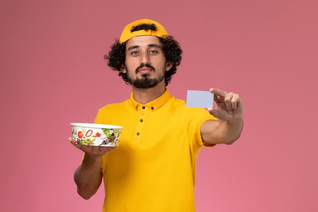 Front view male courier in yellow uniform and cape with round delivery bowl card on his hands on the pink background.