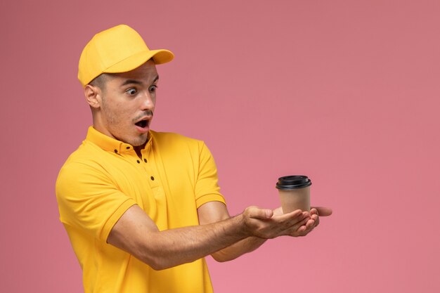 분홍색 배경에 갈색 커피 배달 컵을 들고 노란색 제복을 입은 전면보기 남성 택배